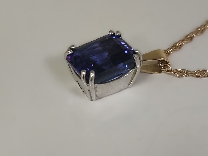 vibrante colgante de Tanzanita talla esmeralda con un rico matiz azul-violeta, engastado en doble garras de oro blanco contrastante, con una valie en oro amarillo y una cadena de oro amarillo.